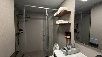 Une salle de bain moderne avec une douche à parois de verre, des toilettes, un lavabo avec un miroir et une étagère avec des serviettes.