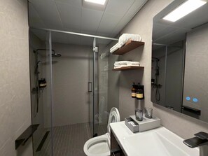 Un baño moderno con ducha envuelta en vidrio, inodoro, lavabo con espejo y estante con toallas.