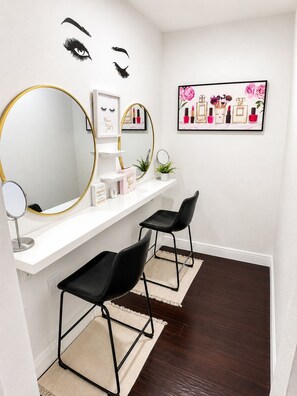 A vanity with a large mirror, two black chairs, and a shelf with cosmetics. - The Velvet Retreat | Glam Escape w/ Beauty Lounge (Tampa)