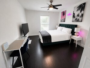 A bedroom with a bed, bedside table, lamp, and a desk with a chair.