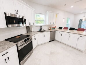 A modern kitchen with white cabinets, stainless steel appliances, and a granite countertop. - The Velvet Retreat | Glam Escape w/ Beauty Lounge (Tampa)