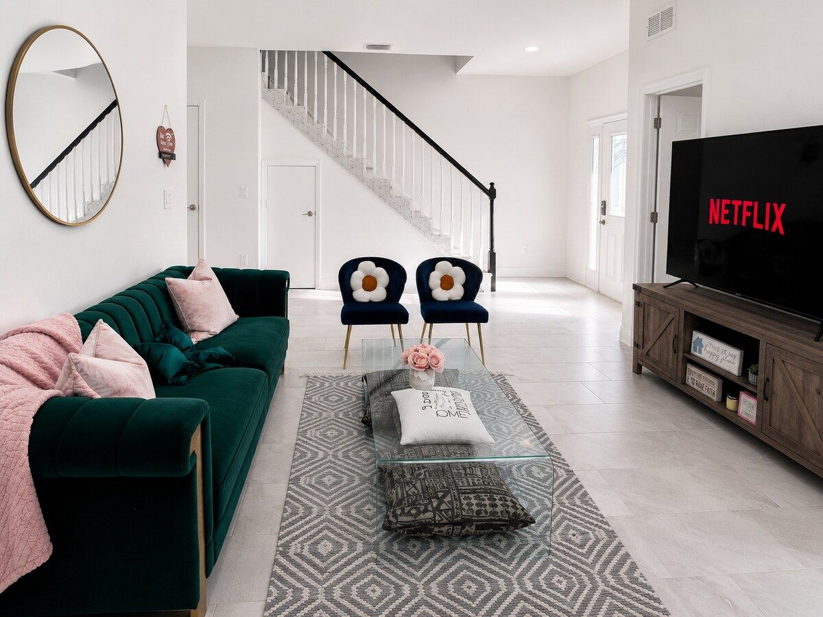 A modern living room with a green sofa, two armchairs, a glass coffee table, and a TV on a wooden stand.