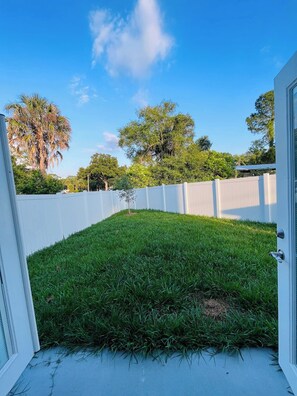 A backyard with a white fence, green grass, and trees in the background.