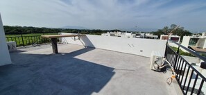 Eine Dachterrasse mit Betonboden, Metallgeländer und Blick auf entfernte Berge.