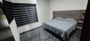 Ein Schlafzimmer mit einem Bett, einem Nachttisch, einem Fenster mit Jalousien und einem Marmorboden.