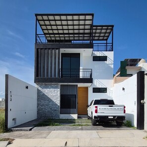 Ein modernes, zweistöckiges Haus mit Solardach, ein weißer Pritschenwagen davor und ein begrenzter Eingangsbereich.