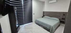 A bedroom with a bed, a nightstand, a TV, and a window with blinds.
