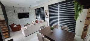 A modern living room with a sofa, dining table, and a TV mounted on a textured wall.