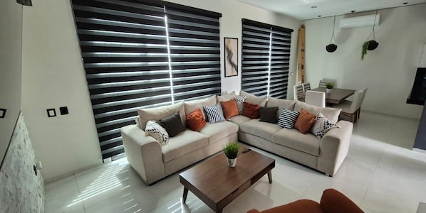A modern living room with a sectional sofa, a coffee table, and a dining area with a table and chairs.