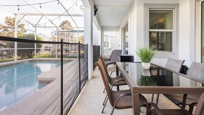 Un'area pranzo esterna moderna con tavolo e sedie in vetro, con vista su una piscina.