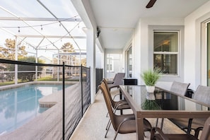 A modern outdoor dining area with a glass table and chairs, overlooking a swimming pool. - Enchanting 6BR Vacation Home w/Pool @Championsgate (Davenport)