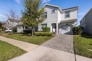 A two-story residential building with a paved driveway, a garage, and a well-maintained lawn. - Enchanting 6BR Vacation Home w/Pool @Championsgate (Davenport)