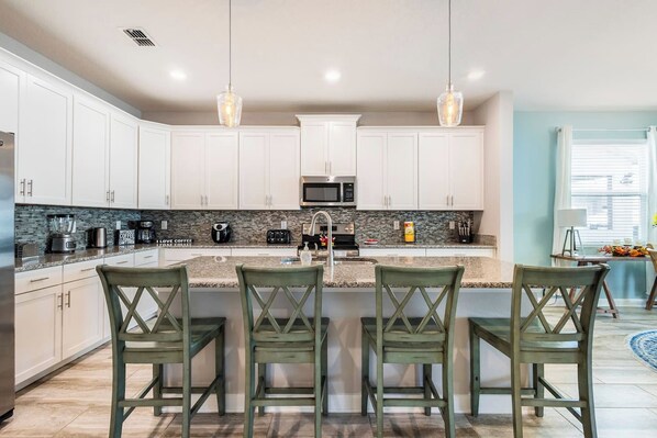 A modern kitchen with white cabinets, a granite countertop, and three bar stools. - Enchanting 6BR Vacation Home w/Pool @Championsgate (Davenport)