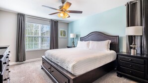 Una camera da letto con un letto, un comodino, una cassettiera, una ventola a soffitto e una finestra con tende.