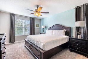 A bedroom with a bed, a nightstand, a dresser, a ceiling fan, and a window with curtains. - Enchanting 6BR Vacation Home w/Pool @Championsgate (Davenport)