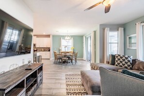 A spacious living room with a large flat-screen TV, a sofa, and a dining area with a chandelier. - Enchanting 6BR Vacation Home w/Pool @Championsgate (Davenport)