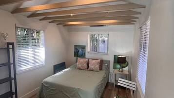 A bedroom with a bed, bedside tables, a radiator, and a window with blinds.