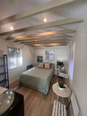 A bedroom with a bed, bedside tables, a radiator, and a window with blinds.