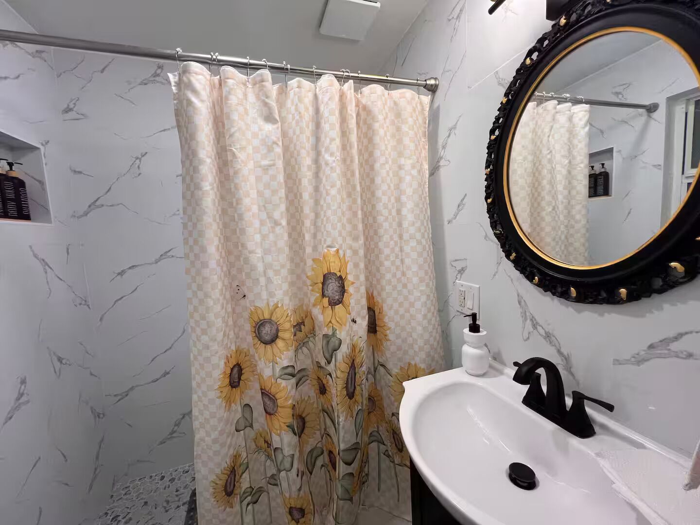 A bathroom with a shower curtain featuring sunflower patterns, a white sink with a black faucet, and a mirror with a black frame.