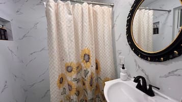 A bathroom with a shower curtain featuring sunflower patterns, a white sink with a black faucet, and a mirror with a black frame.