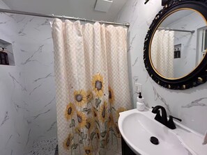A bathroom with a shower curtain featuring sunflower patterns, a white sink with a black faucet, and a mirror with a black frame.