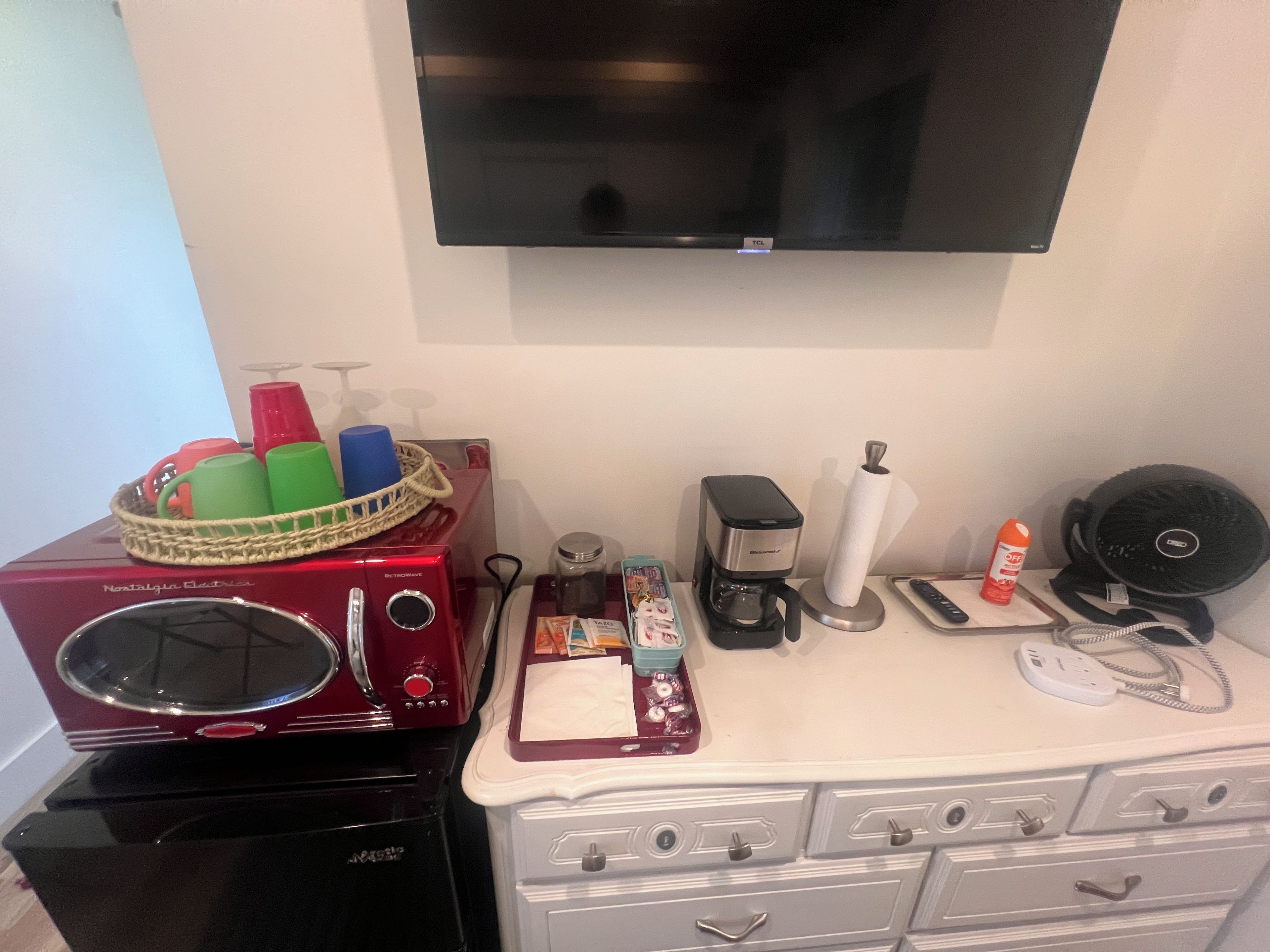 Una kitchenette con estufa roja, cafetera, una cesta con tazas y un televisor de pantalla plana montado en la pared.
