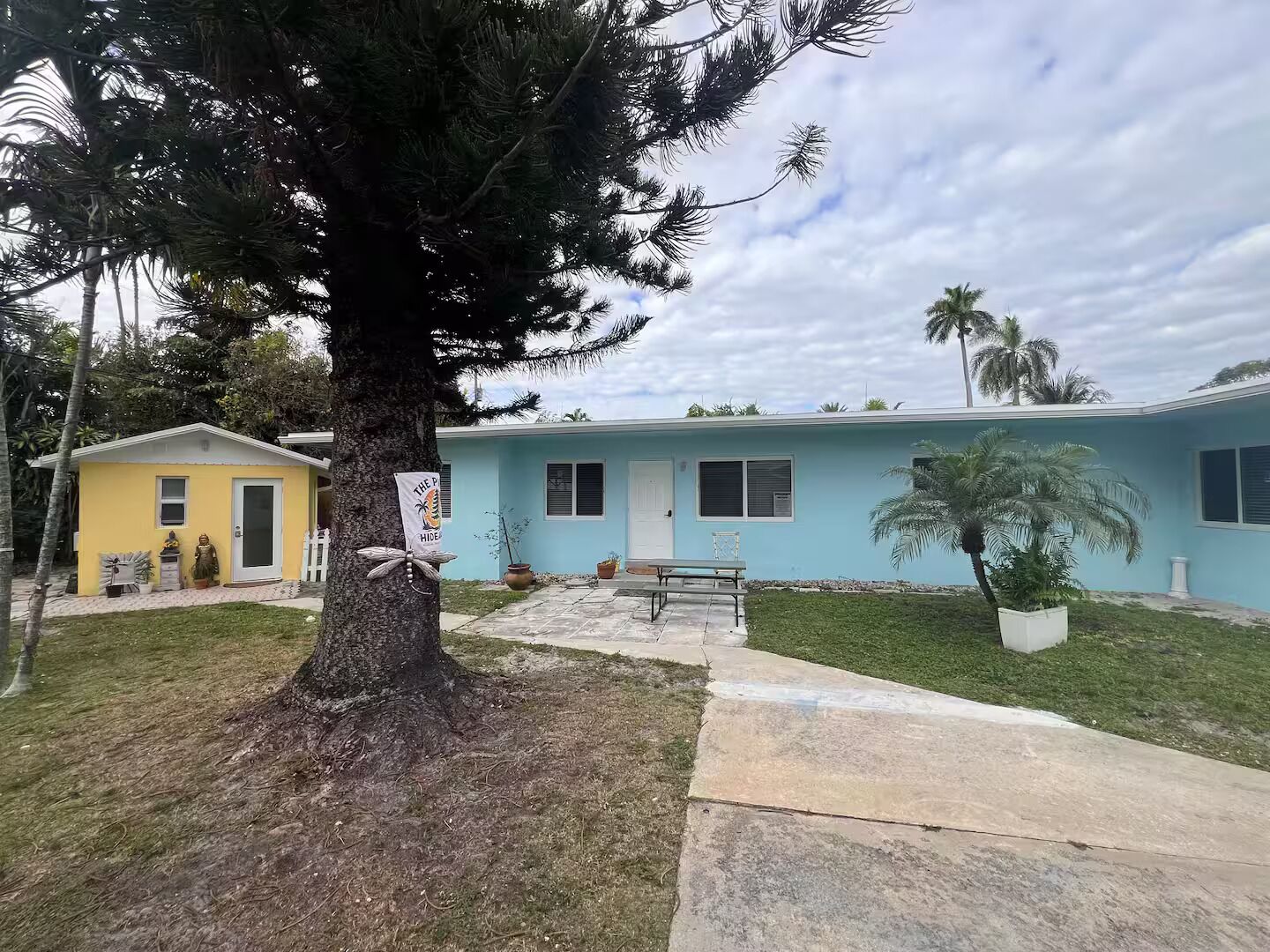 A residential property with a single-story structure, a front yard with a tree, and a small porch area.