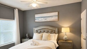 Una camera da letto con un letto, un comodino con una lampada, un tavolino da notte con libri e un quadro appeso al muro.
