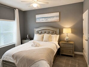 A bedroom with a bed, a bedside table with a lamp, a nightstand with books, and a painting on the wall. -    Family Disney Escape Private Pool + Themed Rooms (Kissimmee)