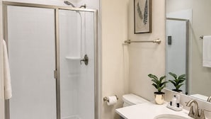 Un bagno moderno con doccia vetro, WC, lavandino con specchio e una pianta in vaso.