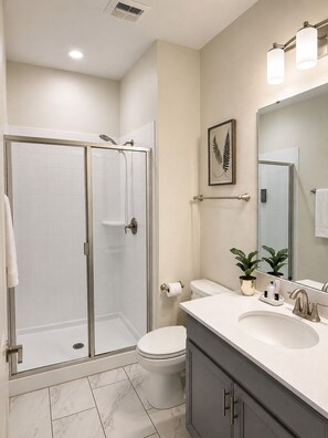 A modern bathroom with a glass-enclosed shower, a toilet, a sink with a mirror, and a potted plant. -    Family Disney Escape Private Pool + Themed Rooms (Kissimmee)
