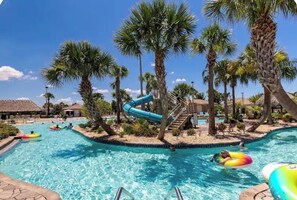 A swimming pool with a water slide surrounded by palm trees and lounge chairs. -    Family Disney Escape Private Pool + Themed Rooms (Kissimmee)