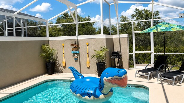 Una piscina interna con uno squalo gonfiabile blu, piante in vaso e sedie a sdraio.