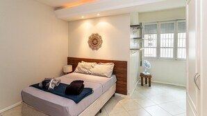 A hotel room with a bed, bedside table, lamp, decorative wall piece, and a window with shutters. - Edificio Aymára (Rio de Janeiro)