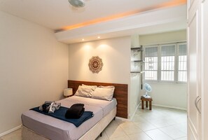 Een hotelkamer met een bed, nachtkastje, lamp, decoratieve wandversiering en een raam met shutters.