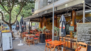 An outdoor cafe with wooden tables and chairs, a menu board, and a chalkboard with prices. - Edificio Aymára (Rio de Janeiro)