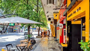 An outdoor café area with tables and chairs, a bicycle, and a tree-lined street. - Edificio Aymára (Rio de Janeiro)