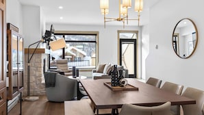 A modern dining area with a wooden table, cushioned chairs, and a chandelier. - Switchback Creek by Sun Peaks Alpine Getaways (Sun Peaks)