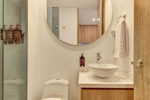 Ein Badezimmer mit rundem Spiegel, Waschbecken in Weiß, Toilette und Duschbereich.