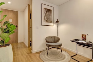 A room with a wooden door, a framed picture on the wall, a chair, a floor lamp, a small table with a bottle, and a potted plant. - w* | Enchanting & Cozy Loft in the Heart of Bogotá (Bogotá)