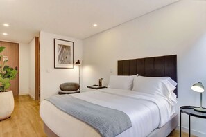 Ein modernes Schlafzimmer mit einem großen Bett, einem Kopfteil, einem Nachttisch, einer Lampe und einem gerahmten Bild an der Wand.