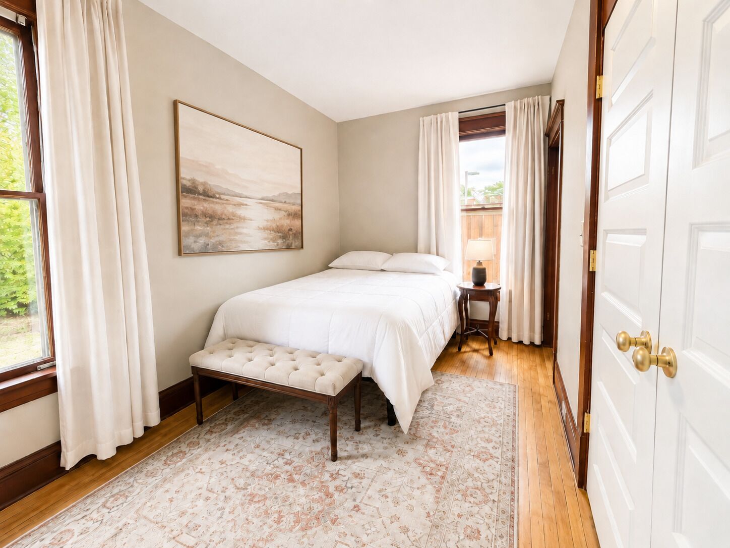 A bedroom with a bed, a bench, a bedside table, a lamp, a painting, and a door.