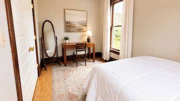 A bedroom with a bed, a desk with a chair, a mirror, a lamp, and a window with curtains.
