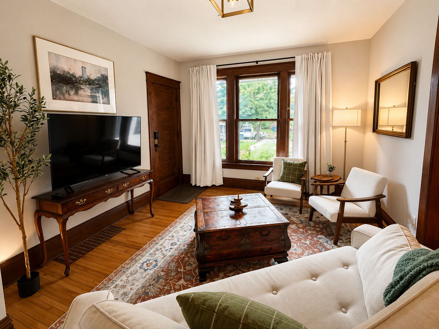 A living room with a television, sofa, armchairs, a coffee table, and a large window with curtains.
