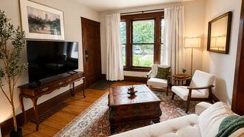 A living room with a television, sofa, armchairs, a coffee table, and a large window with curtains.