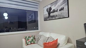 A room with a white leather sofa, a large window, and a framed picture of elephants. - Apartment in Downtown Temuco (Temuco)