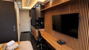 Ein modernes Hotelzimmer mit einem Bett, einem Schreibtisch mit Fernseher und einer Wand mit Holzvertäfelung. Im Hintergrund ist ein Badezimmer zu sehen.