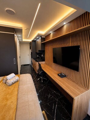 Habitació d'hotel moderna amb un llit, escriptori amb televisió de pantalla plana, paret decorativa de fusta i bany visible al fons.