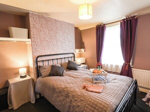 A bedroom with a bed, bedside tables, a lamp, a window with curtains, and a radiator. - 74 Trafalgar Square (Scarborough)
