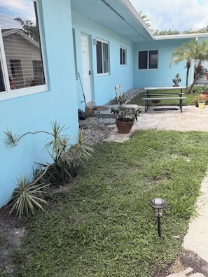 Un edificio azul claro con un patio, una banca y macetas.